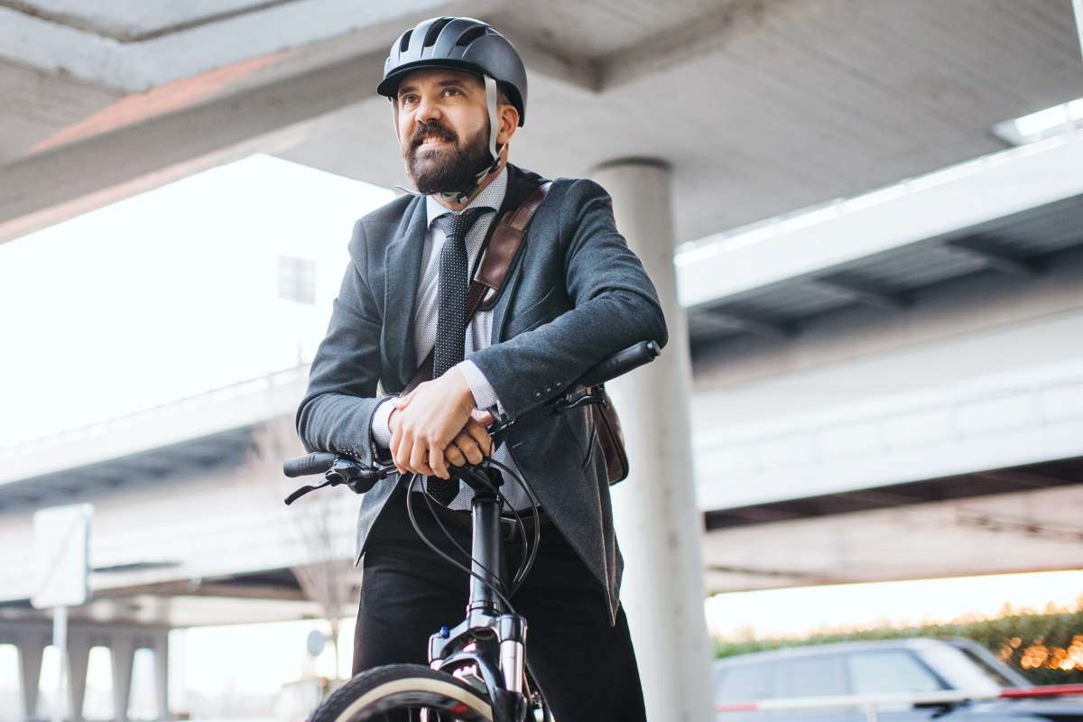 Ein Geschäftsmann in Businesskleidung trägt einen Helm und sitzt auf einem Dienstrad.