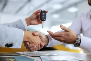 Zwei Personen schütteln sich die Hand, während eine von ihnen den Autoschlüssel übergibt. Dieses Bild symbolisiert den Abschluss eines Leasingvertrages oder die Übergabe eines Firmenwagens, was im Rahmen von Car Allowance-Modellen häufig vorkommt.