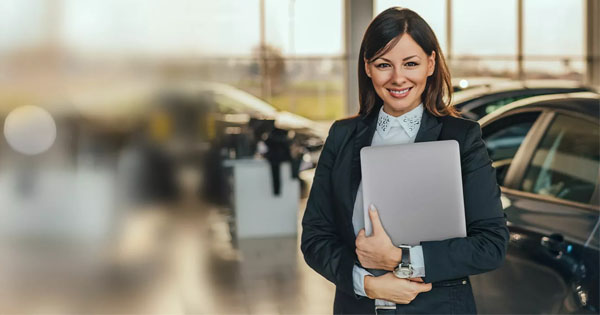 Eine Businessfrau steht in einem hellen Autohaus und hält einen Laptop, während sie die Vorteile der Partnerschaft mit Fleethouse betont, dank der Vertriebsprozesse digitalisiert, Zeit gespart und das Verkaufspotenzial gesteigert werden kann.