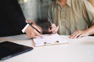 Zwei Personen sitzen an einem Tisch, eine zeigt auf ein Formular, die andere unterschreibt. Das Bild steht für die Dokumentation gesetzlicher Pflichten. Arbeitgeber sind zur regelmäßigen Führerscheinkontrolle verpflichtet – Fleethouse unterstützt mit einer digitalen, rechtskonformen und zeitsparenden Lösung für den Fuhrparkalltag.