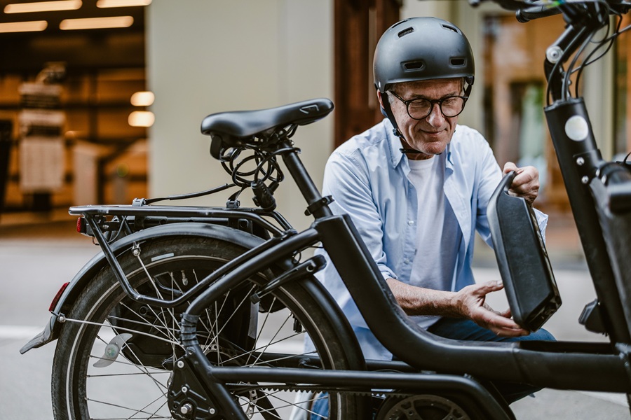 Ein Mann mit Helm und Brille sitzt vor seinem schwarzen E-Bike und hält die Fahrradbatterie in der Hand. Ein Symbolbild für Mobilitätsalternativen im Fleet Management