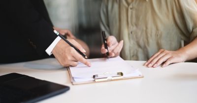 Zwei Personen sitzen an einem Tisch, eine zeigt auf ein Formular, die andere unterschreibt. Das Bild steht für die Dokumentation gesetzlicher Pflichten. Arbeitgeber sind zur regelmäßigen Führerscheinkontrolle verpflichtet – Fleethouse unterstützt mit einer digitalen, rechtskonformen und zeitsparenden Lösung für den Fuhrparkalltag.