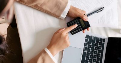 Eine Person berechnet mit Taschenrechner und Laptop die Abschreibung eines Fahrzeugs. Fleethouse unterstützt Fuhrparkverantwortliche mit digitalen Tools und praxisnahen Informationen zur korrekten Abschreibung von Pkw, Lkw und Transportern im Unternehmensfuhrpark.