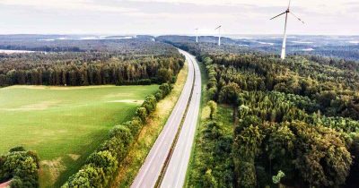 Das Bild zeigt eine weitläufige Straße, gesäumt von Bäumen und Windrädern, die die Nutzung erneuerbarer Energien symbolisieren. Für Unternehmen bietet Fleethouse Lösungen für Fuhrparks mit alternativen Antrieben, um nachhaltige Mobilität zu fördern. So können Sie Ihre Flotte zukunftsfähig und umweltbewusst gestalten.