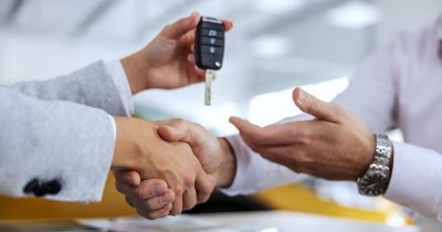 Zwei Personen schütteln sich die Hand, während eine von ihnen den Autoschlüssel übergibt. Dieses Bild symbolisiert den Abschluss eines Leasingvertrages oder die Übergabe eines Firmenwagens, was im Rahmen von Car Allowance-Modellen häufig vorkommt.