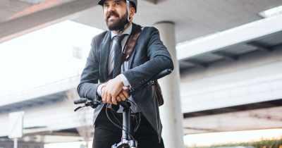 Ein Gesch&auml;ftsmann in Businesskleidung tr&auml;gt einen Helm und sitzt auf einem Dienstrad.
