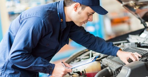 Ein Mechaniker prüft den Motorraum eines Fahrzeugs mit Checkliste in der Hand. Fleethouse unterstützt Fuhrparkleiter bei der digitalen Organisation der UVV-Prüfung – rechtssicher, effizient und jederzeit dokumentiert für maximale Sicherheit im Fuhrparkalltag.