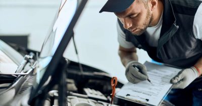 Ein Mechaniker pr&uuml;ft ein Auto und macht Notizen auf einer Werkstatt-Checkliste. Diese ist wichtig, um regelm&auml;&szlig;ig die Wartung und Sicherheit von Fahrzeugen im Fuhrpark zu gew&auml;hrleisten. Eine gute Werkstatt-Checkliste hilft, potenzielle Probleme fr&uuml;hzeitig zu erkennen und Ausfallzeiten zu minimieren.